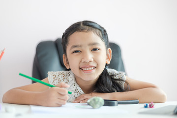 Little Asian girl using the pencil to write on the paper doing homework for education concept select focus shallow depth of field