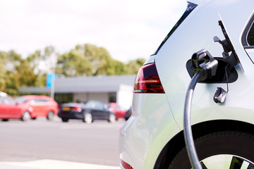Close Up Of Power Cable Charging Electric Car Outdoors In Supermarket Car Park