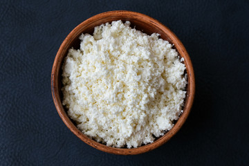 Cottage cheese in a brown bowl on a dark background. Dietary food with calcium.
