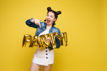 Fototapeta na wymiar Attractive happy woman laughing holding big gold letters posing at yellow studio background medium long shot. Beautiful fashionable young girl relaxing having positive emotion