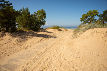 Road with tire marks sprinkled with sand going to the sea through the dunes