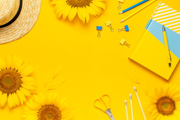 Top view flat lay of workspace desk styled design with sunflowers, straw hat, notebook, diary, pencils, pen scissors on bright yellow background. Autumn or summer Concept. Sunflower natural background