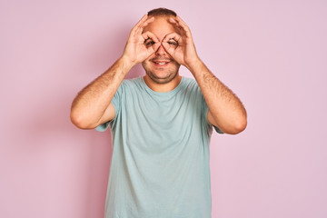 Fototapeta premium Young man wearing blue casual t-shirt standing over isolated pink background doing ok gesture like binoculars sticking tongue out, eyes looking through fingers. Crazy expression.