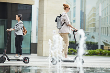 Full length portrait of people commuting in city, focus on young woman riding electric scooter in foreground, copy space