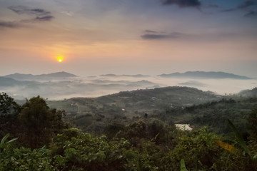 Fototapeta premium Mountain view misty morning of top hills and green forest around with sea of fog with yellow sun light in the sky background, sunrise at ITTI View Point, Khao Kho, Phetchabun, Thailand.