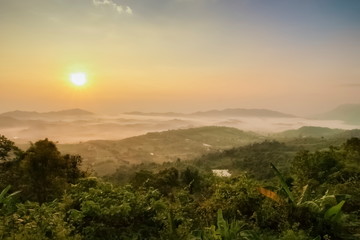 Fototapeta na wymiar Mountain view misty morning of top hills and green forest around with sea of fog with yellow sun light in the sky background, sunrise at ITTI View Point, Khao Kho, Phetchabun, Thailand.