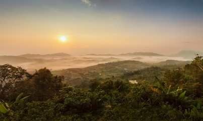 Mountain view panorama misty morning of top hills and green forest around with sea of fog with yellow sun light in the sky background, sunrise at ITTI View Point, Khao Kho, Phetchabun, Thailand.