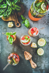 Homemade fresh strawberry and basil lemonade or ice tea in glass tumblers with eco-friendly plastic-free straws and ingredients over dark grey table background, top view. Cold summer soft drink