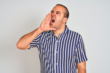 Young man wearing blue striped shirt standing over isolated white background shouting and screaming loud to side with hand on mouth. Communication concept.