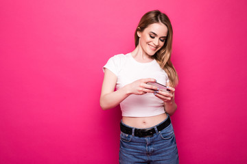 Pretty young teenage girl typing and reading text message on her new modern cell phone mobile on a pink background
