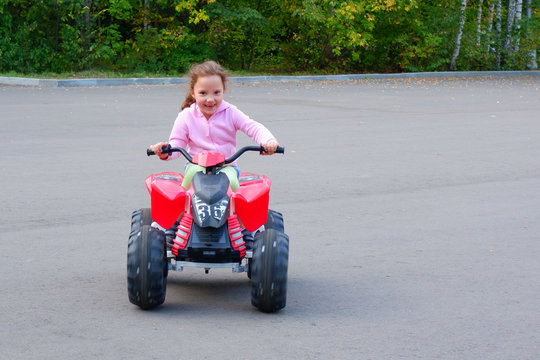 Little girl is riding on a electric quadricycle. Children's summer vacation and entertainments.