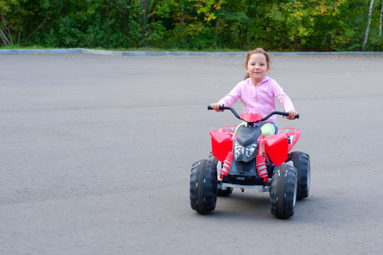 Little girl is riding on a electric quadricycle. Children's summer vacation and entertainments.