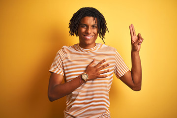 Afro man with dreadlocks wearing striped t-shirt standing over isolated yellow background smiling...