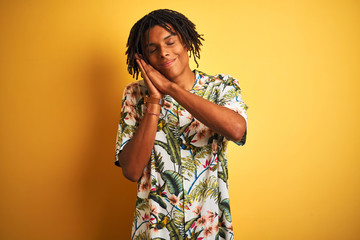 Afro man with dreadlocks on vacation wearing summer shirt over isolated yellow background sleeping tired dreaming and posing with hands together while smiling with closed eyes.