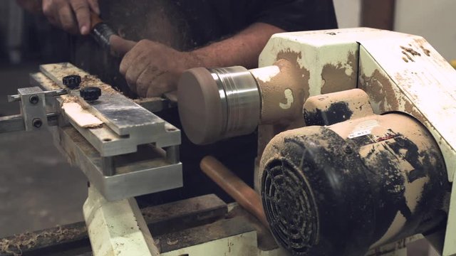 Laborer carving a round wooden disk on a lathe with sawdust stabilized slider shot
