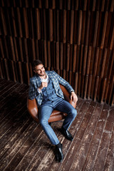 Young successful businessman in a blue suit in a cage is sitting in a leather chair. young man with a beard smiling and looks into the distance