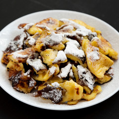 Homemade german Kaiserschmarrn pancake on a white plate on a black surface, low angle view.