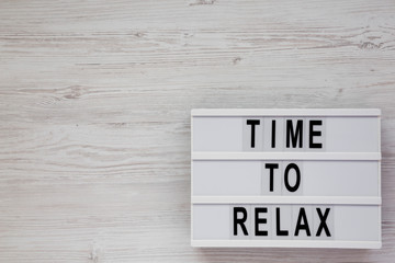 'Time to relax' words on a lightbox on a white wooden background, top view. Overhead, from above. Flat lay. Copy space.