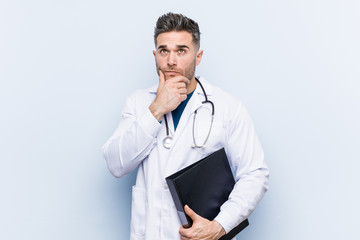 Caucasian doctor man holding a folder looking sideways with doubtful and skeptical expression.