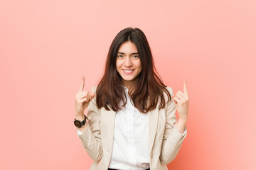 Young brunette business woman against a pink background indicates with both fore fingers up showing...