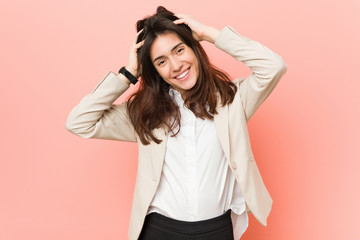 Naklejka premium Young brunette business woman against a pink background laughs joyfully keeping hands on head. Happiness concept.
