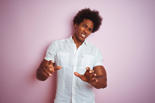 Young american man with afro hair wearing white shirt standing over isolated pink background disgusted expression, displeased and fearful doing disgust face because aversion reaction
