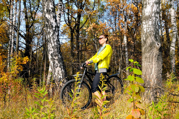 Naklejka premium Young slim girl on a bicycle in autumn birch forest