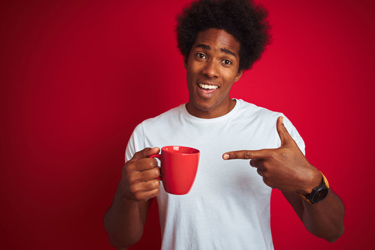 Young african american man drinking a cup of coffee standing over isolated red background very happy pointing with hand and finger
