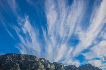 Dramatic blue sky with streaks of vertical clouds over mountain range.