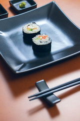 Sushi maki rolls presented on a plate with sauces and chopsticks