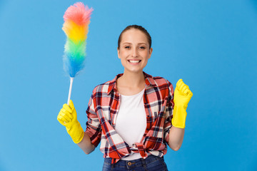 Portrait of happy housewife wearing yellow rubber gloves holding colorful duster while doing housework and cleaning room