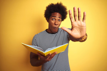 Afro american student man reading book standing over isolated yellow background with open hand...