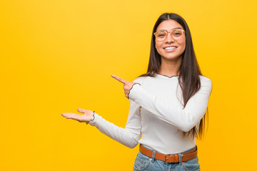 Young pretty arab woman against a yellow background excited holding a copy space on palm.
