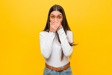 Young pretty arab woman against a yellow background shocked covering mouth with hands.