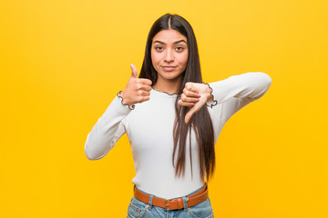 Young pretty arab woman against a yellow background showing thumbs up and thumbs down, difficult...