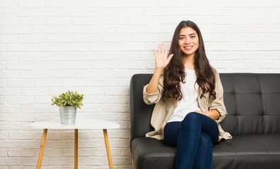 Young arab woman sitting on the sofa smiling cheerful showing number five with fingers.