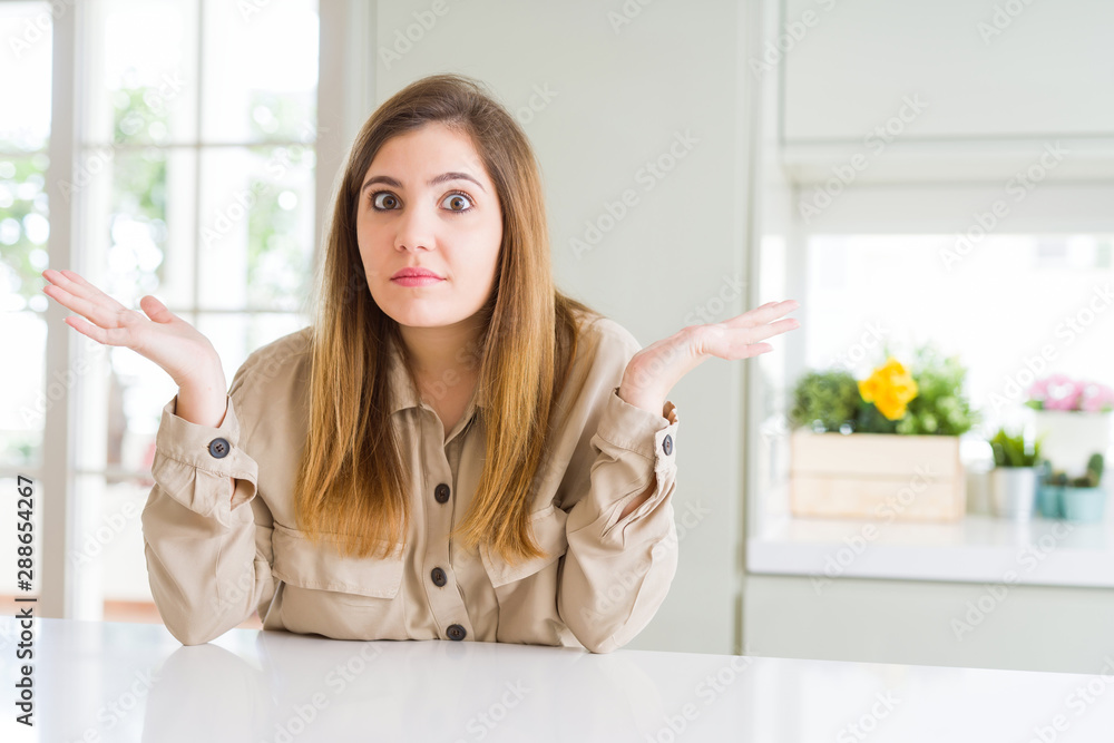 Sticker beautiful young woman at home clueless and confused expression with arms and hands raised. doubt con