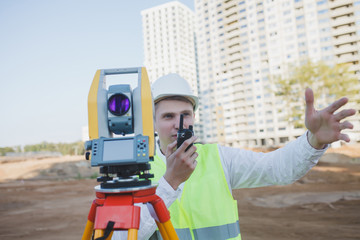 Surveyor equipment. Surveyor engineer in protective wear using geodetic equipment, holding walkie...