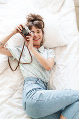 Happy cheery positive woman indoors at home lies on bed in the morning holding camera photographing.