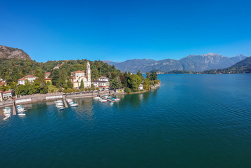 Naklejka na ściany i meble Aerial view landscape on beatiful Lake Como in Tremezzina, Lombardy, Italy. Scenic small town with traditional houses and clear blue water. Summer tourist vacation on rich resort with nice harbour