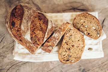 Brown fresh bread with seeds are cut into pieces on old wood background. Top view, copy space