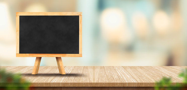 wood table with blank blackborard menu and blurred leaf foreground leaf in restaurant with bokeh background. product display template.Business presentation