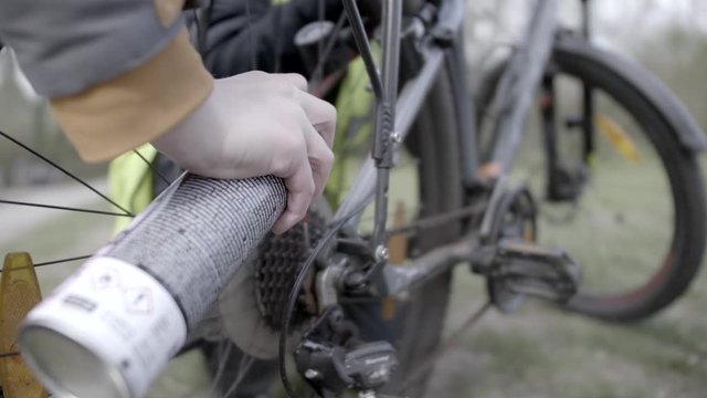 Close up on womans hand with spray greasing chain on bicycle