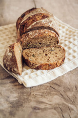 Brown fresh bread with seeds are cut into pieces on old wood background. Top view, copy space