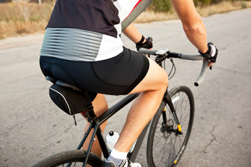 Fototapeta premium The cyclist is training on his road bike outside the city by asphalt road