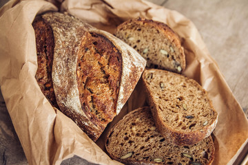 Brown fresh bread with seeds are cut into pieces on old wood background. Top view, copy space