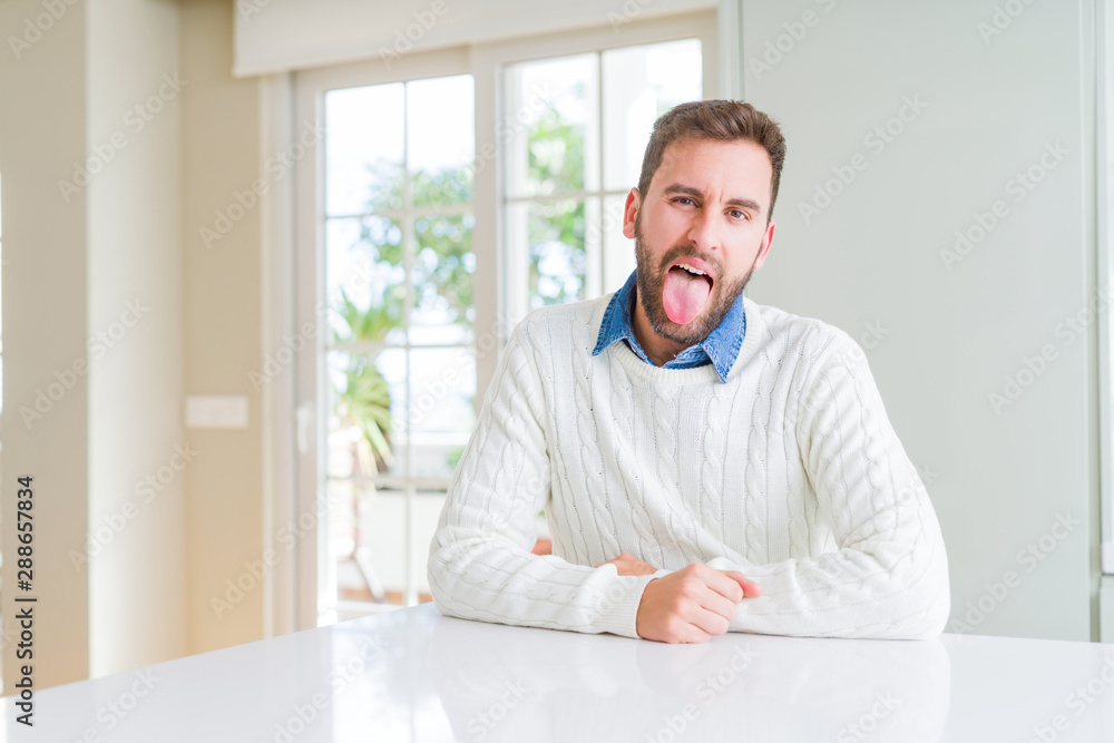 Wall mural Handsome man wearing casual sweater sticking tongue out happy with funny expression. Emotion concept.