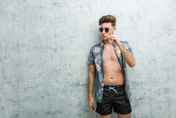 Fototapeta na wymiar Young caucasian man wearing a swimsuit showing number one with finger.