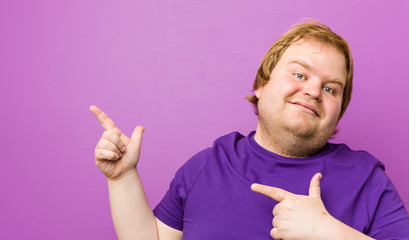 Young authentic redhead fat man pointing with forefingers to a copy space, expressing excitement...