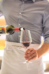 Midsection of waiter pouring red wine in wineglass at restaurant